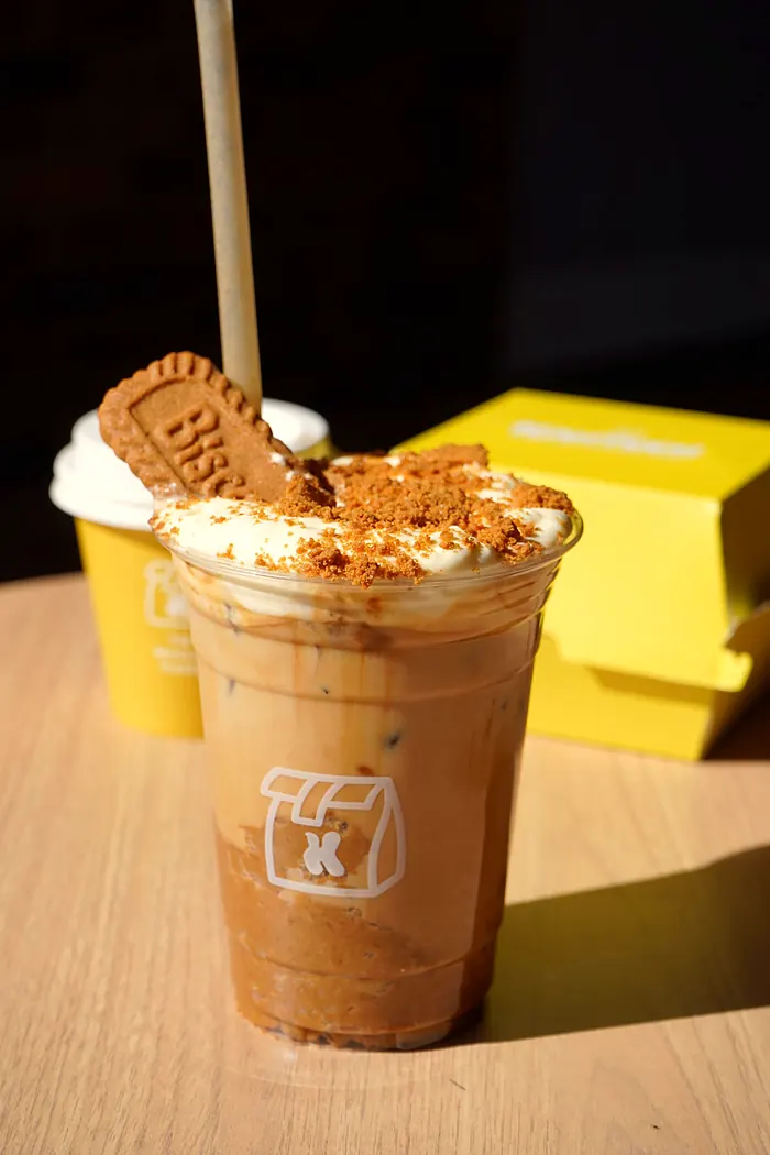 Iced coffee topped with cream and a biscuit next to a Kanteen box