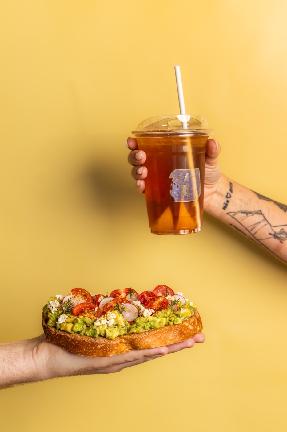 Avocado toast and an iced tea held over a yellow background